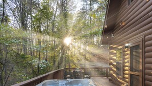 A hot tub on a wooden deck with a forest view, a table with chairs, and a log cabin structure. - Moon Lake Retreat - Kayaks, Fishing, Private shoreline, Hot tub, Room to Roam (Blue Ridge)