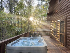 A hot tub on a wooden deck with a forest view, a table with chairs, and a log cabin structure. - Moon Lake Retreat - Kayaks, Fishing, Private shoreline, Hot tub, Room to Roam (Blue Ridge)