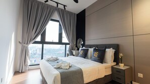 A modern hotel room with a large bed, grey curtains, a view of the city, and a nightstand with a lamp. - Skyline KL by Guestonic (Kuala Lumpur)