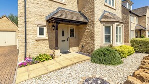 A stone building with a front door, a mailbox, and a small garden with flowers and shrubs. - Old Railway Close (Lechlade)