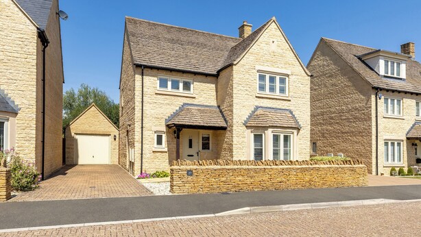 A row of stone houses with pitched roofs, a paved driveway, and a stone wall with a number '27' visible. - Old Railway Close (Lechlade)