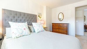 A bedroom with a large bed, a dresser, a mirror, and a painting on the wall. - Old Railway Close (Lechlade)