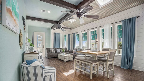 A spacious living room with a dining area, wooden floors, ceiling fans, and large windows with curtains. - Beachside Vibes (Galveston)