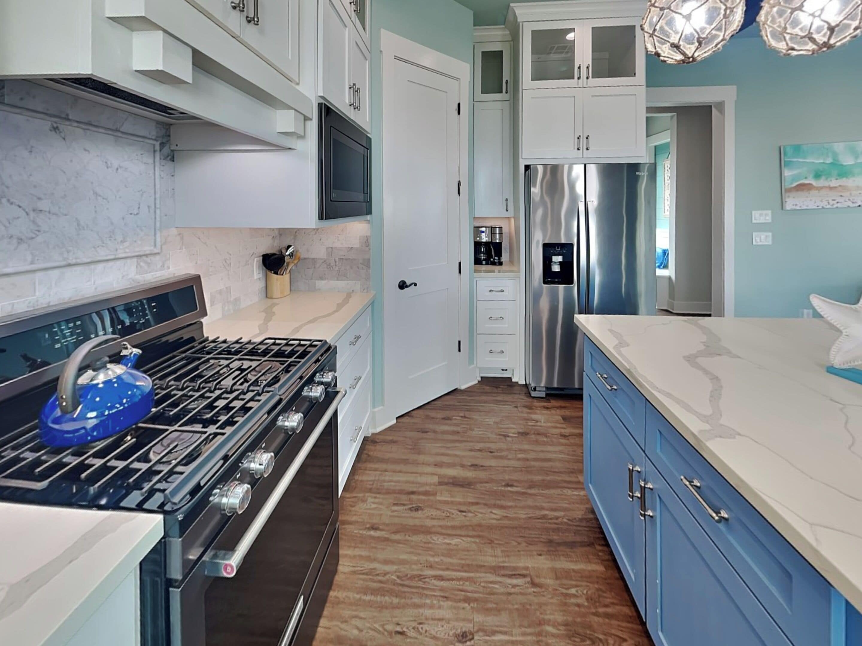 A modern kitchen with a stainless steel refrigerator, a blue kettle, and white cabinetry.