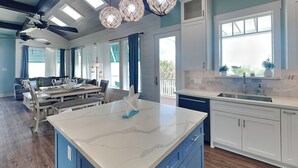 A modern kitchen with a large island, blue cabinets, and a dining area with a table and chairs. - Beachside Vibes (Galveston)