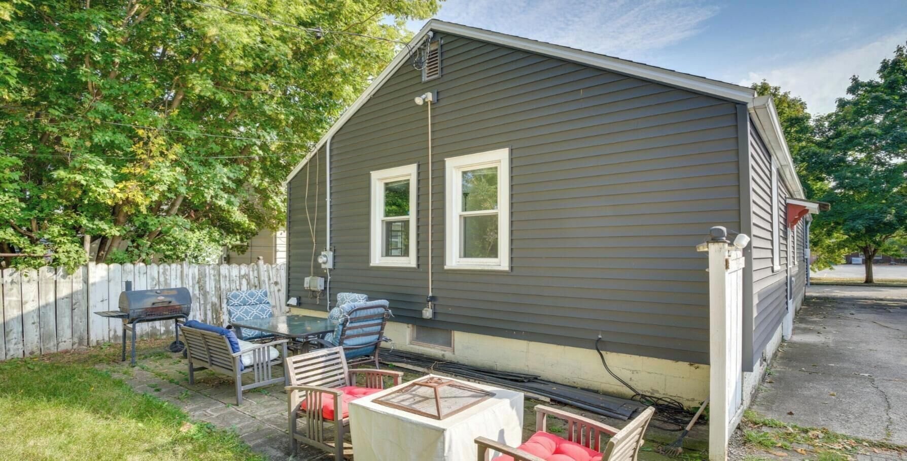Une petite maison dotée d’un patio, d’un barbecue et de mobilier d’extérieur.