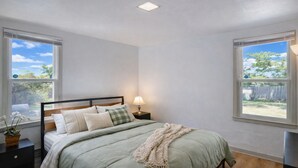 A bedroom with a bed, nightstands, a lamp, and windows with a view of the outdoors.