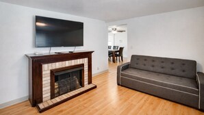 A living room with a flat-screen TV, a fireplace, a sofa, and a dining area in the background.