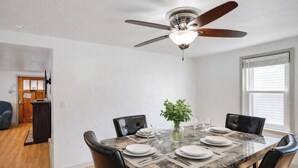 A dining area with a table set for four, a ceiling fan, and a window with blinds.