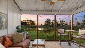 Un espacio al aire libre cubierto con sofá, sillas y una mesa, con vistas a un campo verde y una masa de agua.