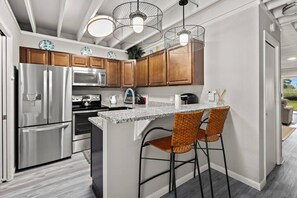 A modern kitchen with stainless steel appliances, wooden cabinets, and a granite countertop. - Cozy Beach Escape Mallard Lakes Resort Amenities (Selbyville)