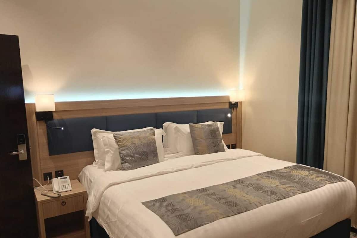 Una habitación de hotel con una cama, lámparas de noche, un teléfono en la mesita de noche y una cortina.