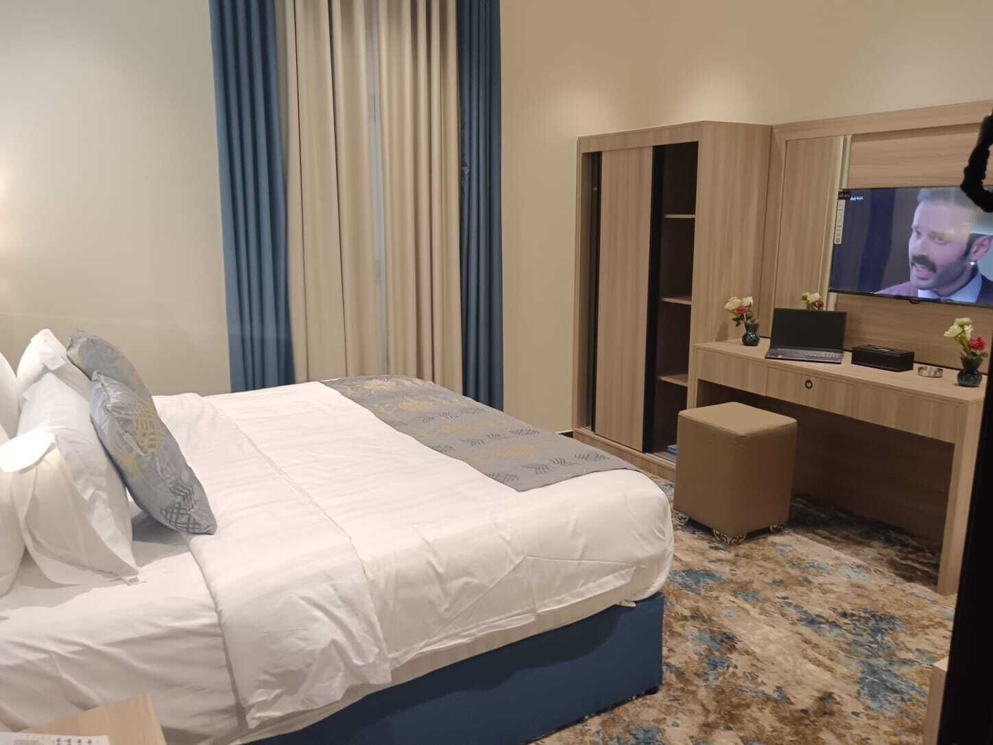 A hotel room with a bed, a desk with a laptop, a TV, and a wardrobe.