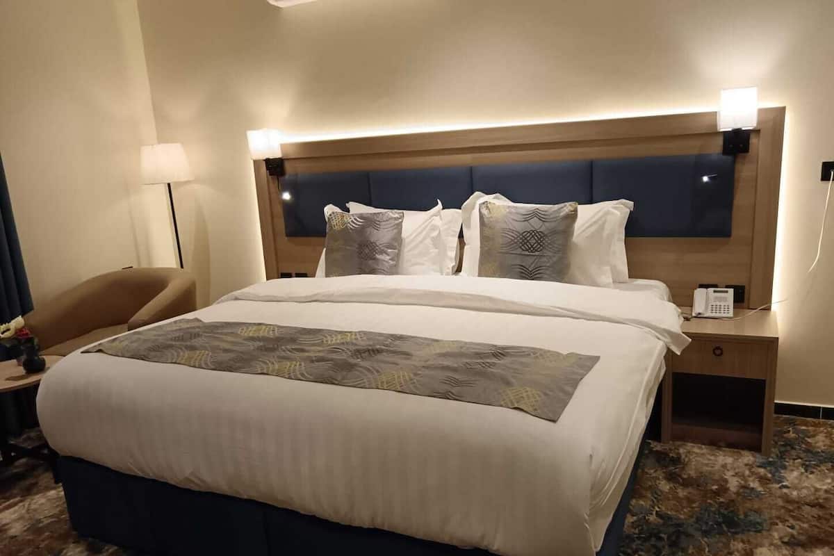 Una habitación de hotel con una cama grande, una mesita de noche con teléfono, una silla y una lámpara.