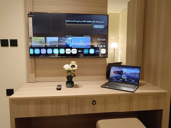 A hotel room with a wooden desk, a laptop, a remote control, and a vase with flowers. - Fursan Al Arab Serviced Apartments (Jeddah)