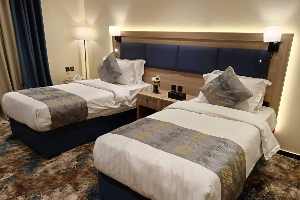 Dos camas con cabeceras, mesitas de noche, lámparas y un arreglo floral.