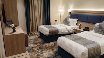 A hotel room with two beds, a desk with a laptop, a lamp, and a nightstand.