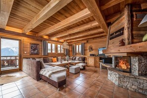 A log cabin interior with a fireplace, wooden beams, a sofa, and a dining area. - Chalet in Village With Bars and Shops Nearby (Huez)