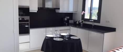 A modern kitchen with white cabinets, a black countertop, and a dining table set for four.