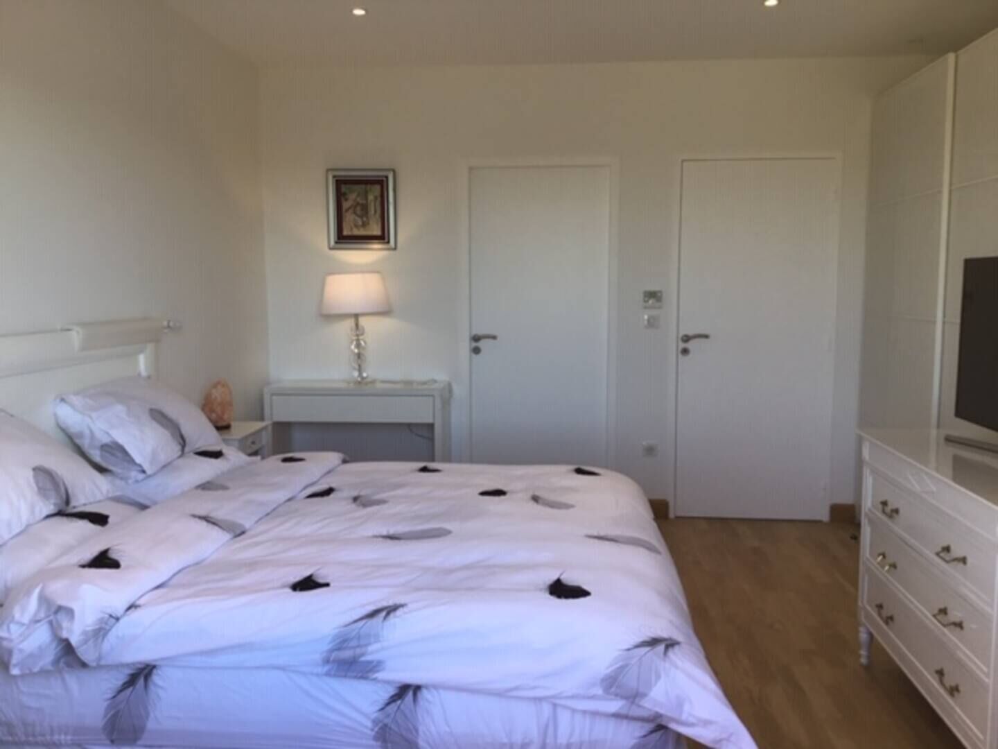 Une chambre à coucher avec un lit, une table de chevet avec une lampe, une commode et une porte.