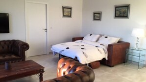 Ein Zimmer mit einem Bett, einem braunen Ledersofa, einem kleinen Tisch und einem Glastisch mit einer Lampe.
