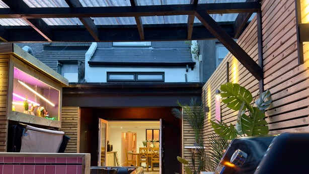 Une terrasse extérieure couverte, équipée d’un barbecue, d’un coin salon et offrant une vue sur l’intérieur de la maison.