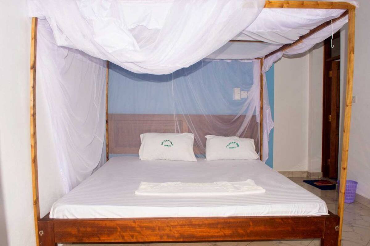 Een eenpersoonsbed met houten frame, wit beddengoed en een klamboe.
