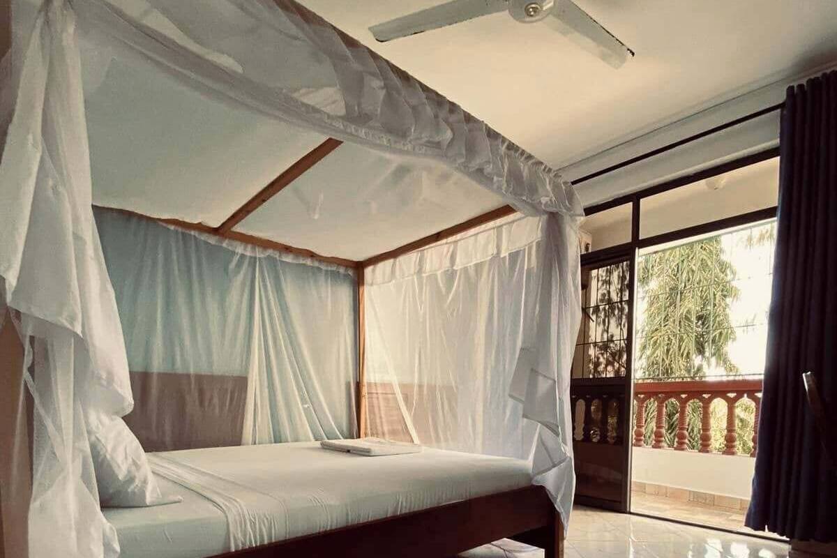 Een slaapkamer met een bed, een plafondventilator en een balkon met uitzicht.