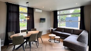 A modern room with a dining table, chairs, a sofa, and a TV. - Lodge 65 | 6 persoons chalet in Zennewijnen (Zennewijnen)
