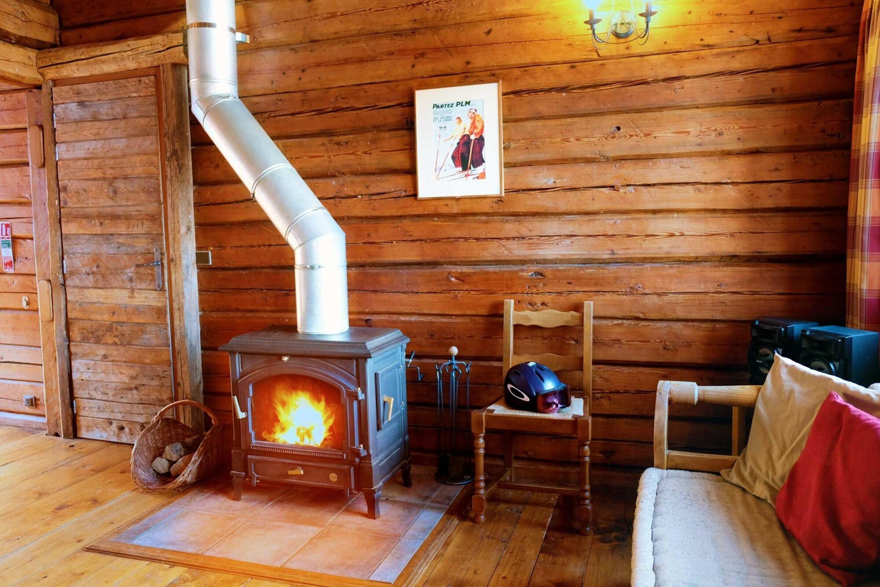 Un acogedor interior de cabaña con una estufa de leña, un sillón, un sofá y un póster en la pared.