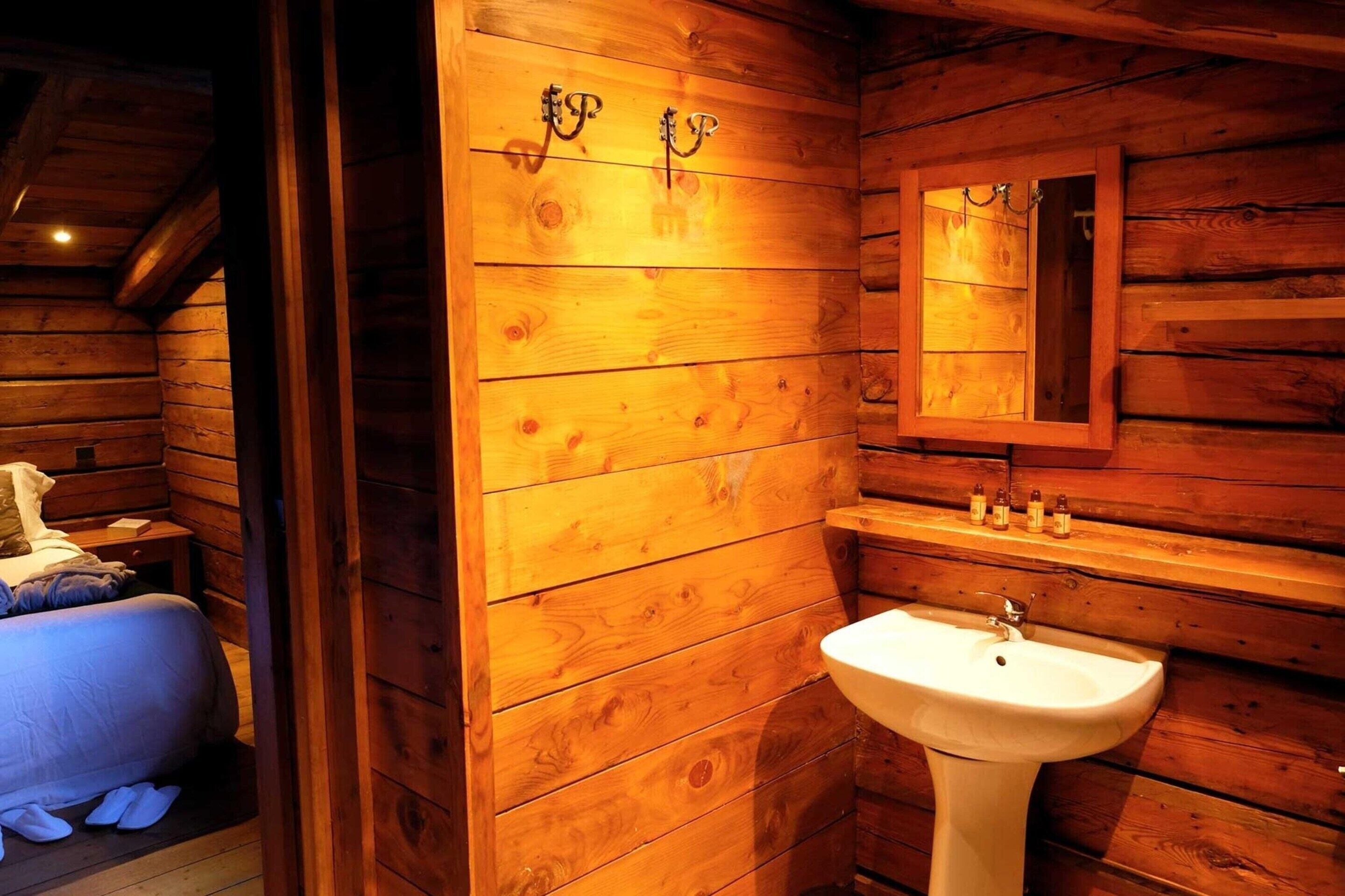 A wooden cabin interior with a bed, a sink, and a mirror.