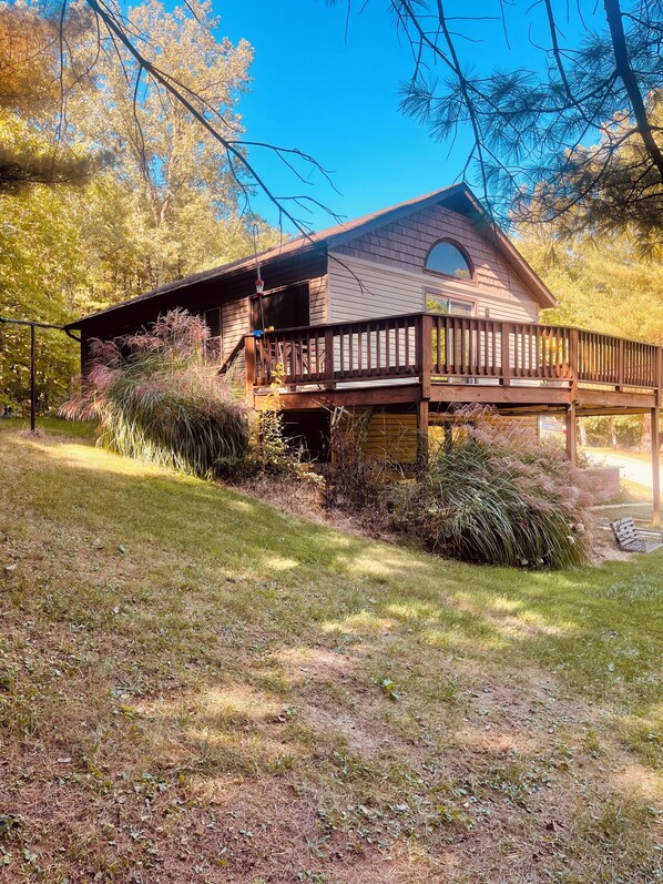 A wooden cabin with a deck, surrounded by trees and grass.