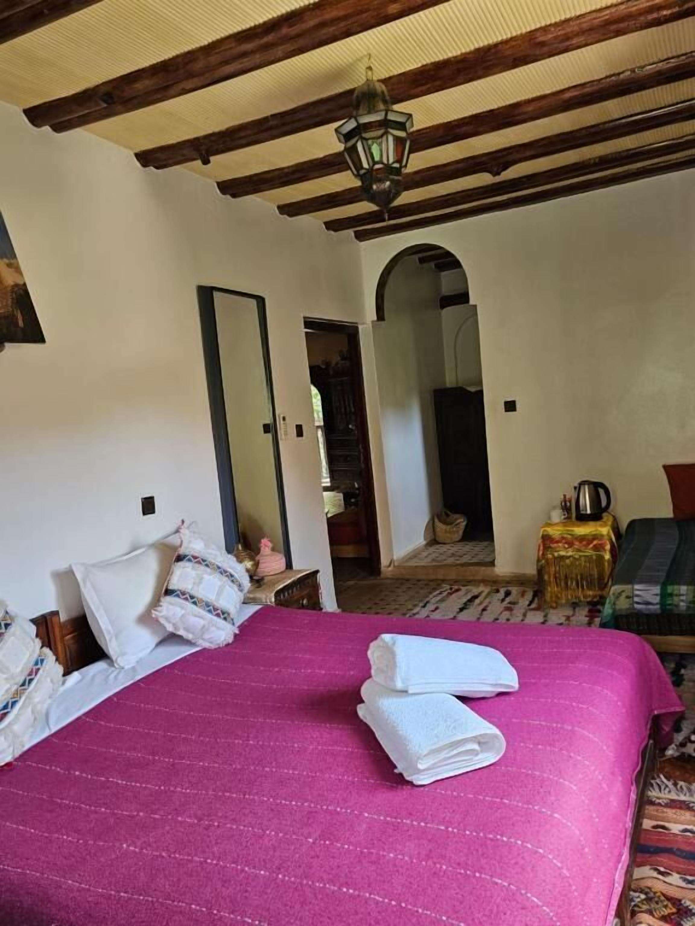 A bedroom with a bed, a mirror, a door, and a hallway leading to another room.