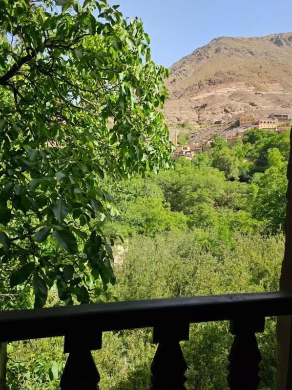 A view of a mountainous landscape with dense greenery and a building in the distance. - Riad Oussagou (Imlil)