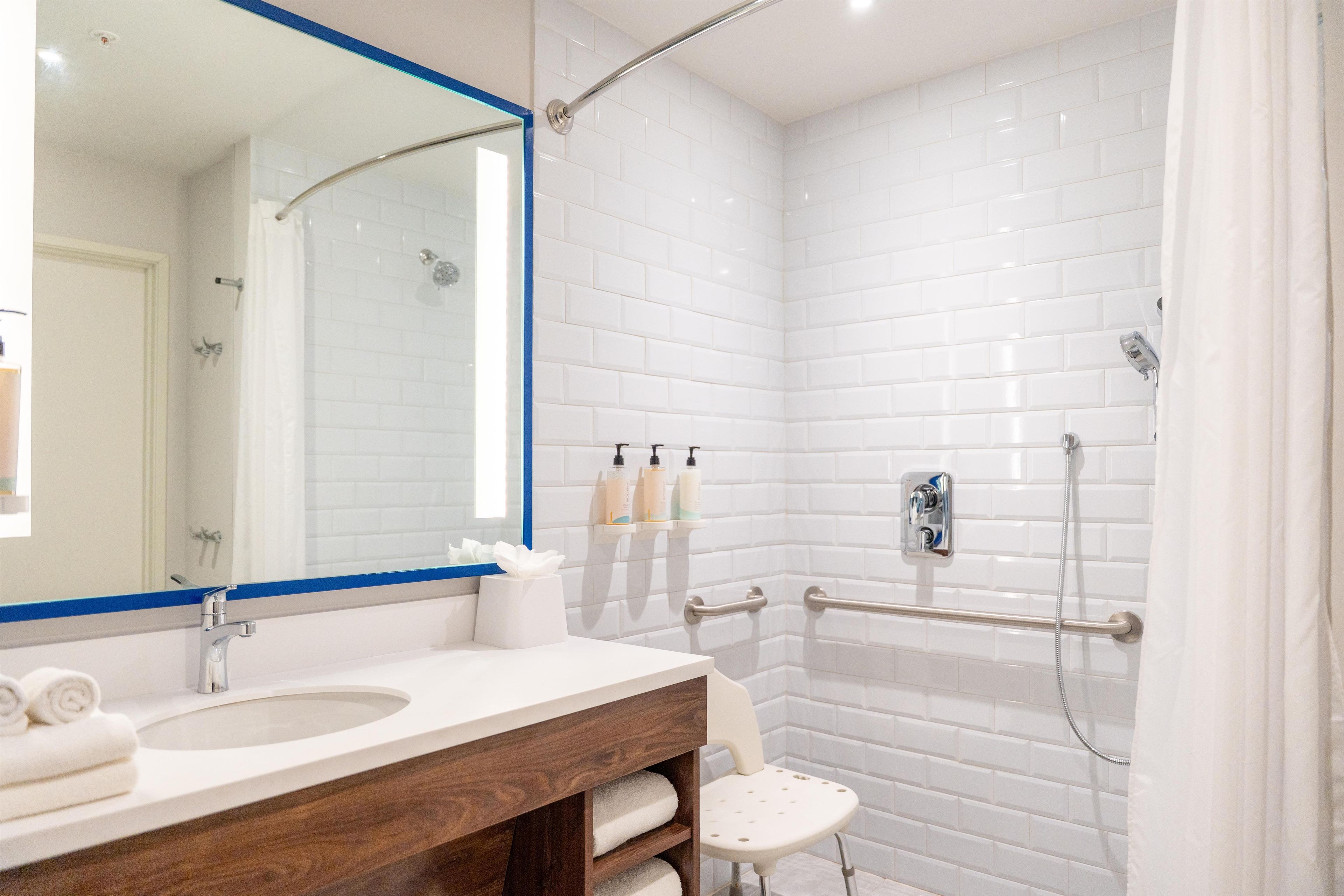 A modern bathroom with a white-tiled shower, a vanity with a mirror, and a small stool.