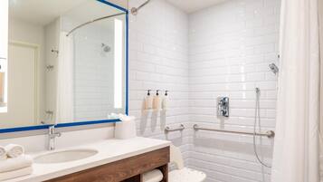 A modern bathroom with a white-tiled shower, a vanity with a mirror, and a small stool.