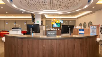 A hotel reception desk with a digital display, a sign for room rates, and a sign indicating a guest service area.