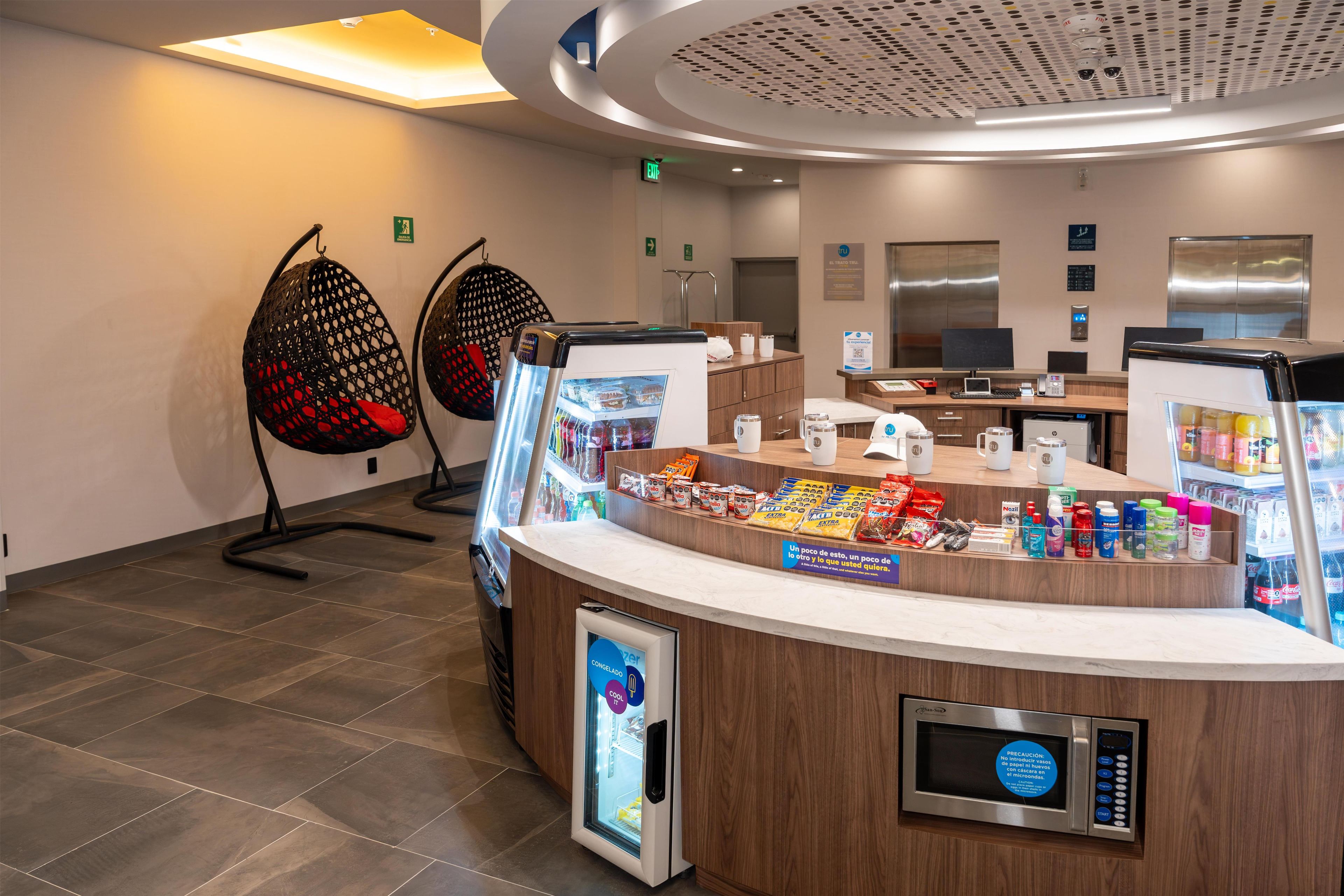 Zona de recepción de un hotel con estación de autoservicio para bebidas, área de estar y un diseño de techo moderno.