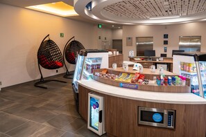 Un espace d’accueil d’hôtel doté d’un coin boissons en libre-service, d’un espace détente et d’un design moderne au niveau du plafond.
