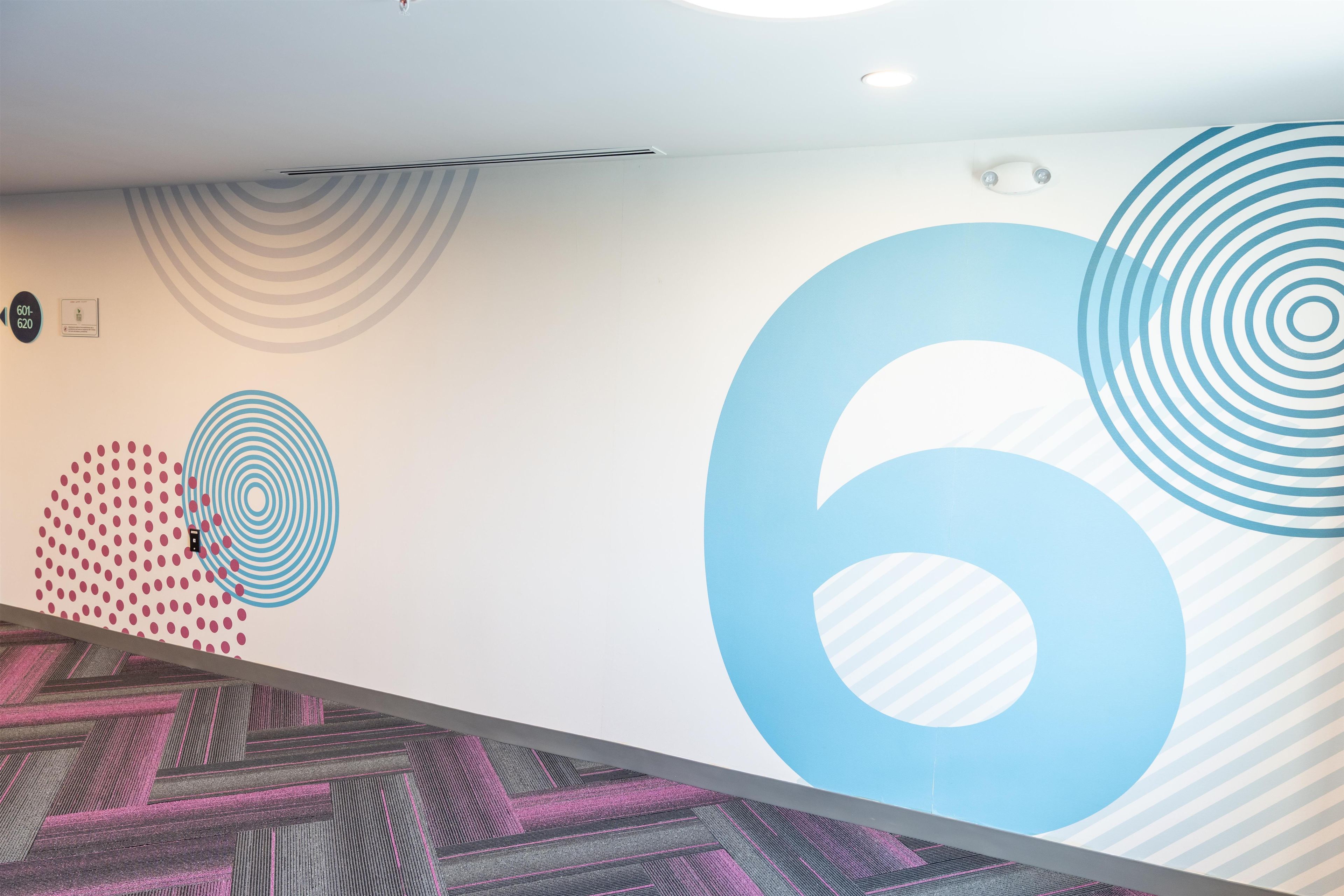 Un intérieur moderne avec un grand chiffre « 6 » peint sur le mur, une moquette à motifs et un plafond doté d’un éclairage encastré.