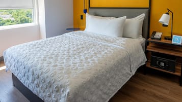 A neatly made bed with a textured white bedspread, a bedside table with a lamp, and a nightstand with a phone and a QR code.