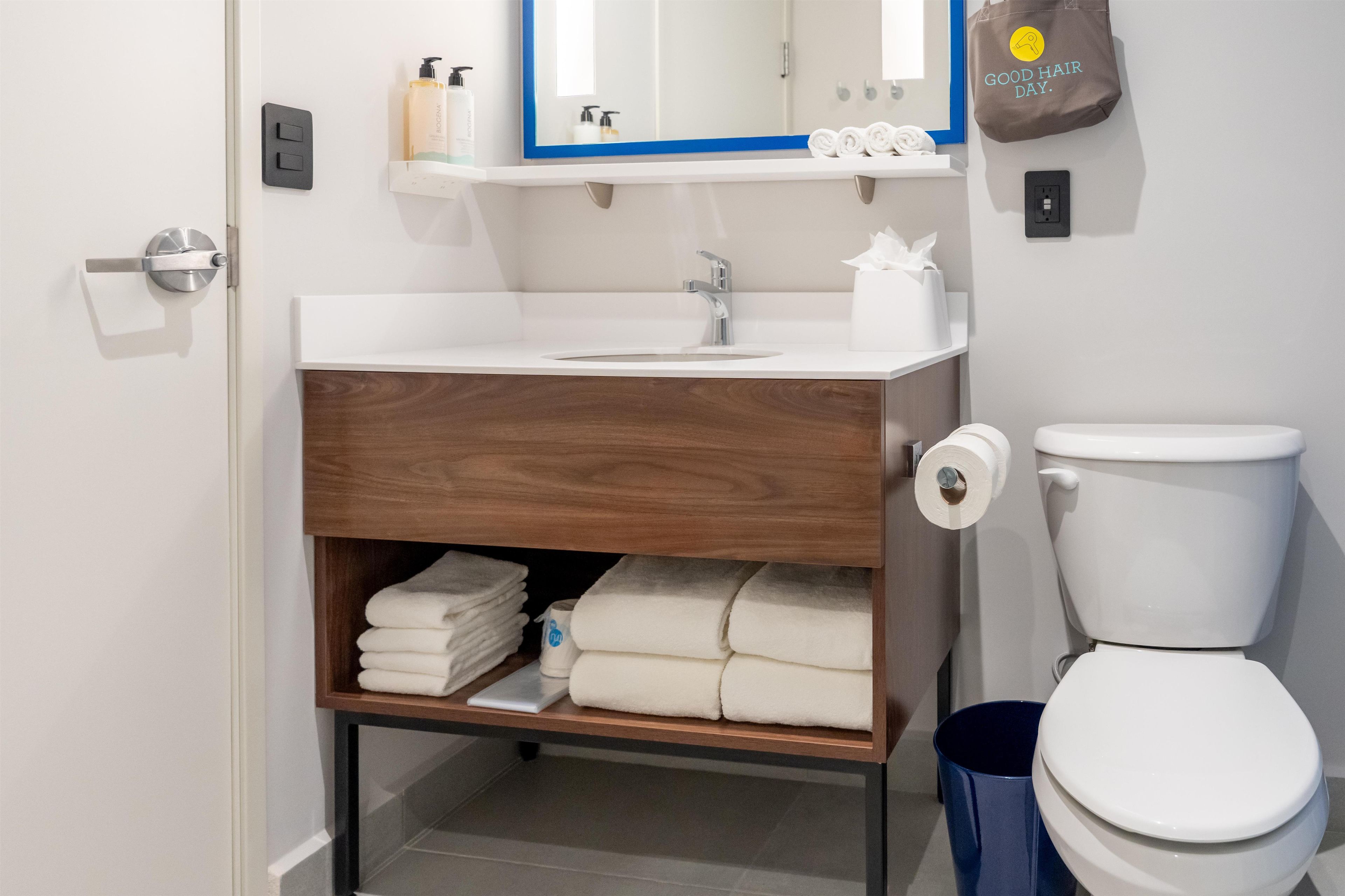 A modern bathroom with a white sink, a mirror, a toilet, and a shelf with towels.