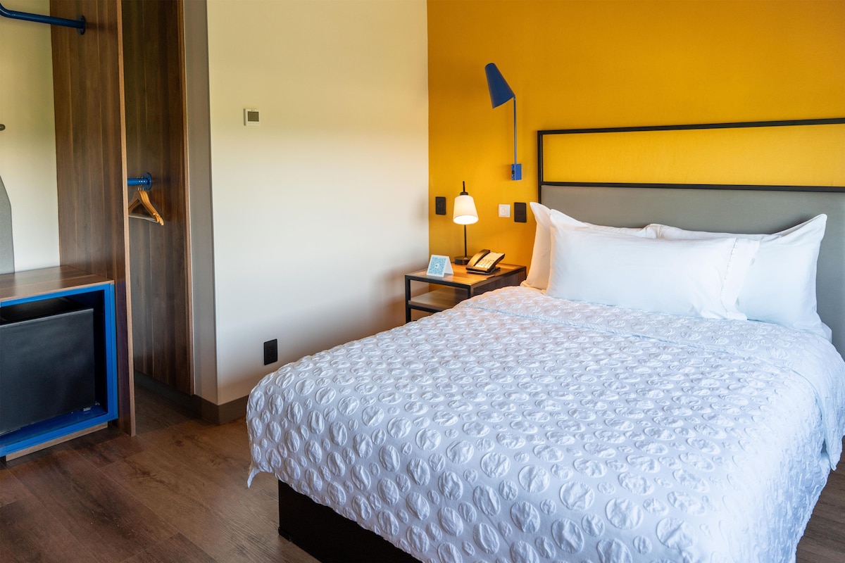 Ein Hotelzimmer mit Bett, Nachttisch, Lampe und einem Holztisch.