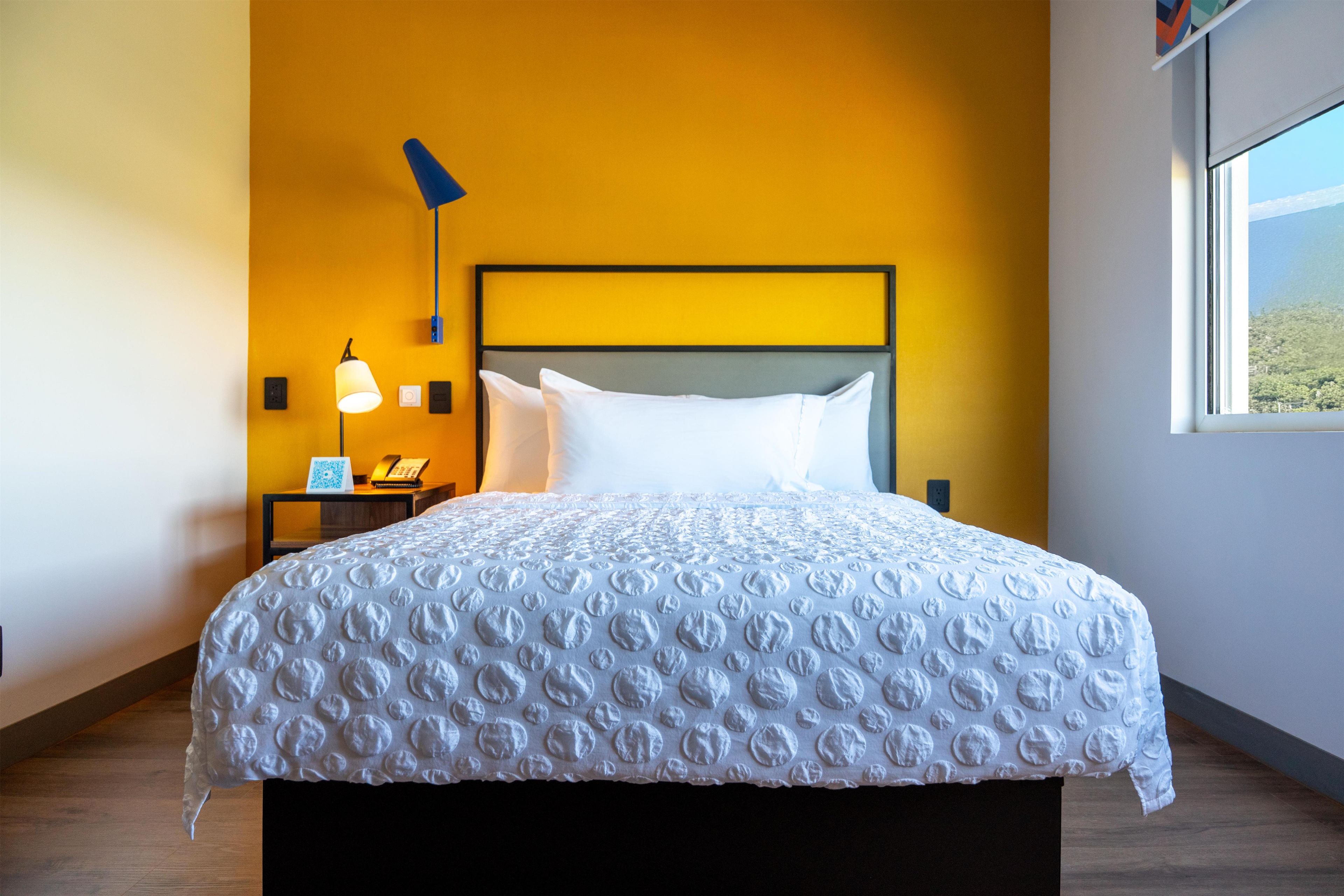 A hotel room with a large bed, a nightstand with a lamp, and a window with a view.