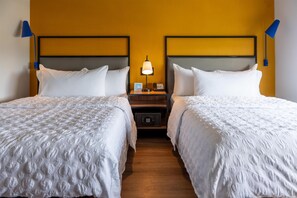 Een hotelkamer met twee bedden, een nachtkastje met een lamp, een telefoon en een QR-code.