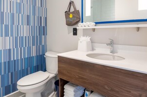 A modern bathroom with a white toilet, a sink with a mirror above it, and a towel rack with a brown tote bag hanging on it.