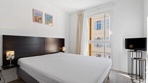 A hotel room with a large bed, a TV, and two wall-mounted lamps. - Air-conditioned flat with a balcony & swimming pool (Grasse)