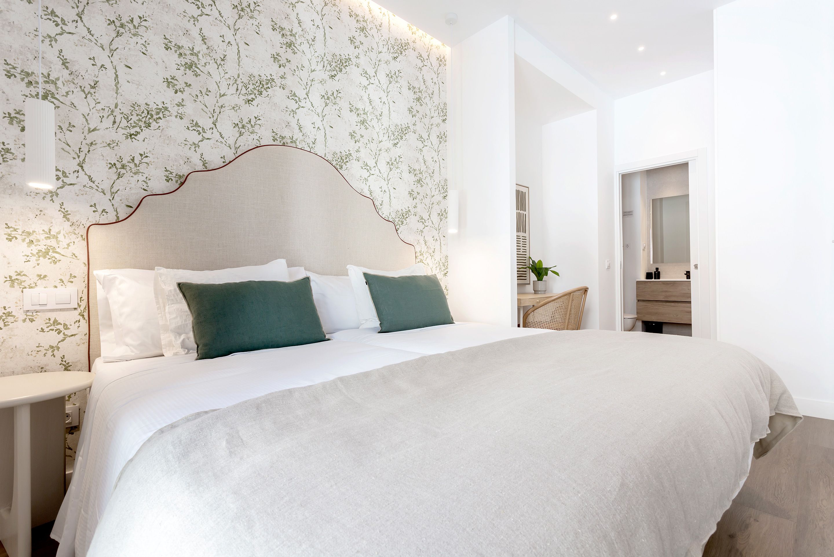 A modern bedroom with a large bed, a headboard with a leaf pattern, and a nightstand with a lamp.