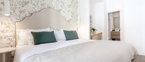 A modern bedroom with a large bed, a headboard with a leaf pattern, and a nightstand with a lamp.