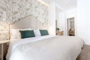 Un dormitorio moderno con una cama grande, un cabecero con estampado de hojas y una mesita de noche con lámpara.